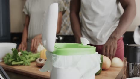 mid section of african american couple throwing food waste out in ktichen in slow motion