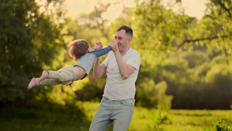 loving father smiles walking with the child sitting on the neck at sunset on a meadow in summer in slow motion.