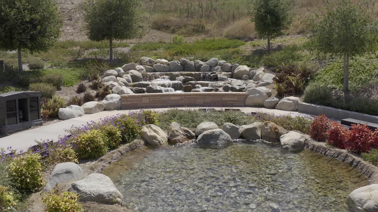 캘리포니아 장례식장에서 편안한 자연 정원에서 작은 폭포 위를 날아다니는 느린 공중 촬영