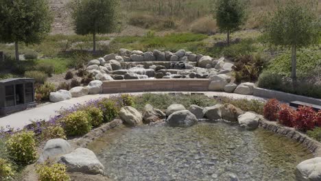 Slow-aerial-shot-flying-over-a-small-waterfall-in-a-relaxing-nature-garden-at-a-California-mortuary