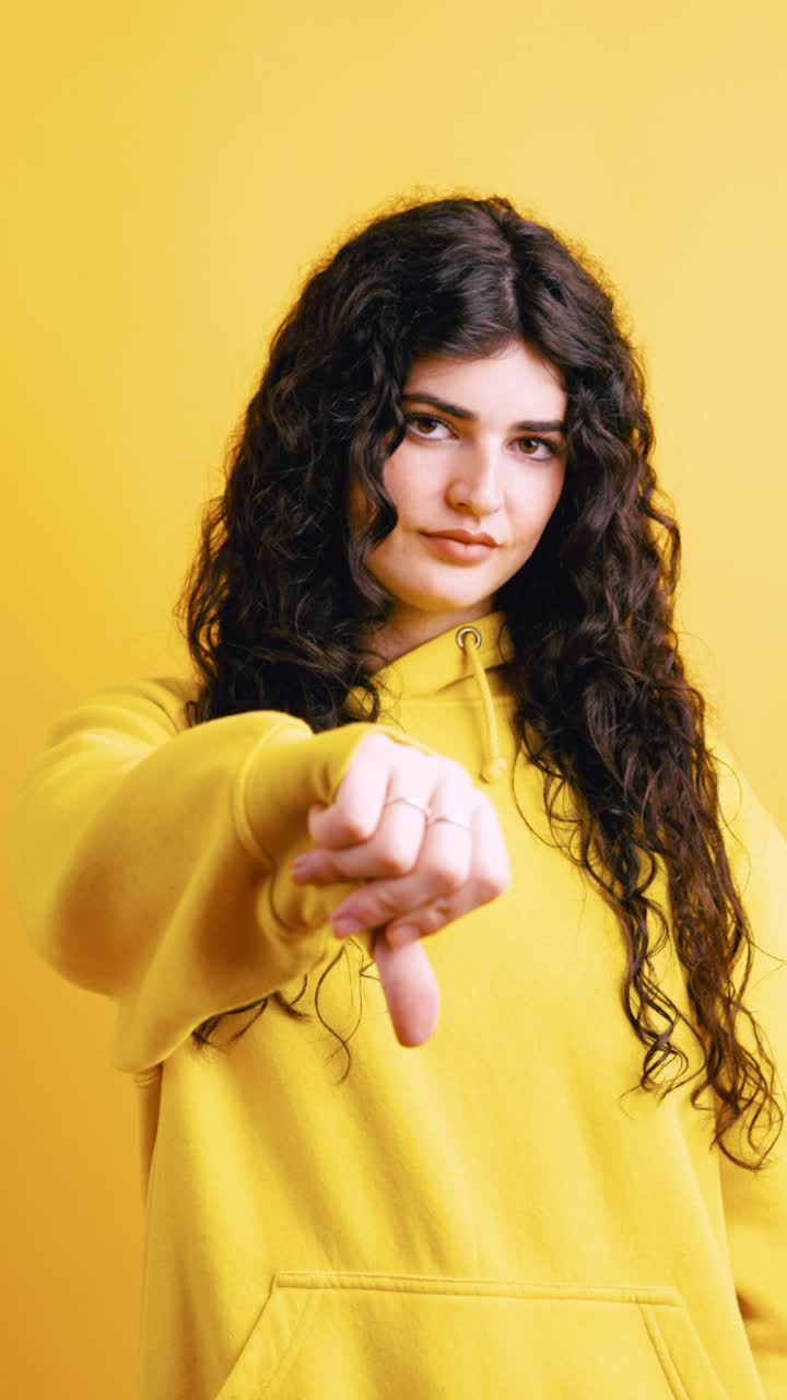 Woman giving thumbs down on yellow background