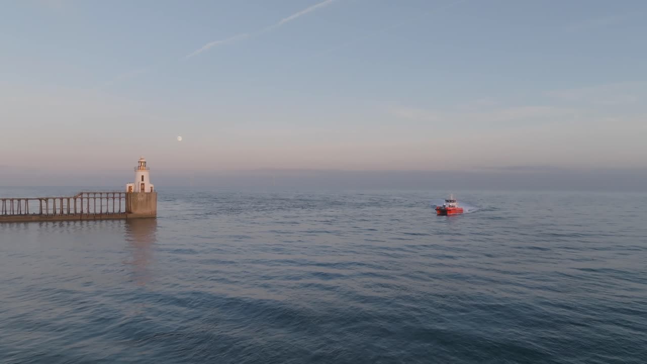 Sunset clip showing fishing boat returning to harbour around lighthouse, in Northumberland England