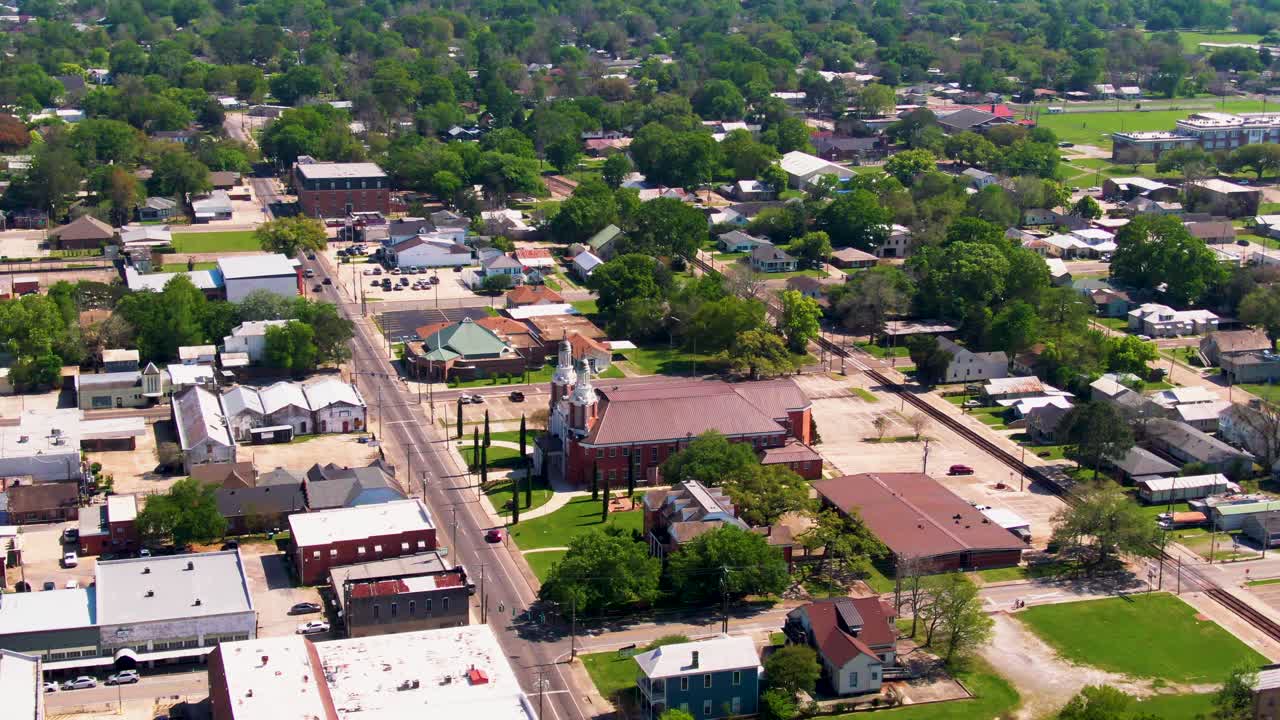 A drone shot of New Iberia, Louisiana, looking down St. Peter Street with views of St. Peter Catholic Church, First Baptist Church, railroad tracks, local businesses, and greenery