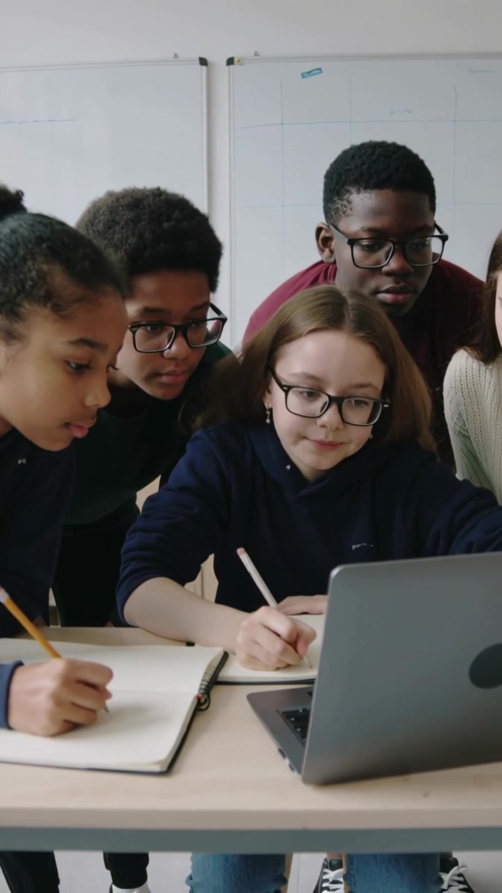 Vertical video: Collaborating five students writing at laptop in classroom, studying with notebooks