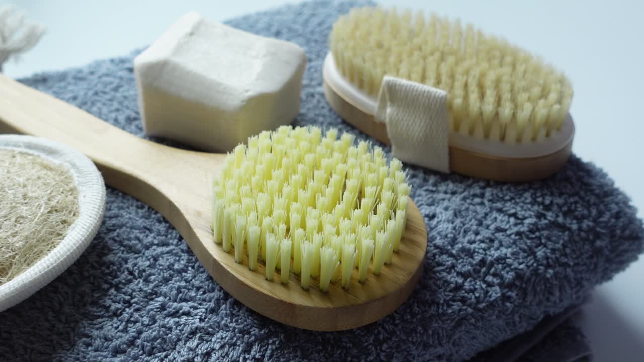 Bir havlu üzerinde vücut fırçası, banyo lifi ve sabun.