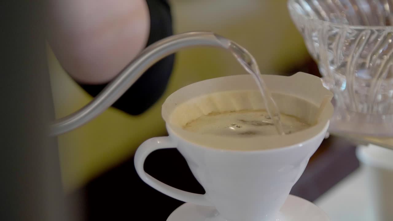 The barista, using a metal kettle, pours water into a container with a filter
