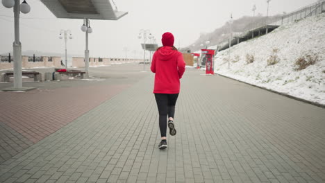 back view of coach jogging outdoors on interlocked pavement during winter, serene environment with modern urban features including benches, snow, a snowy hill, and lamp posts