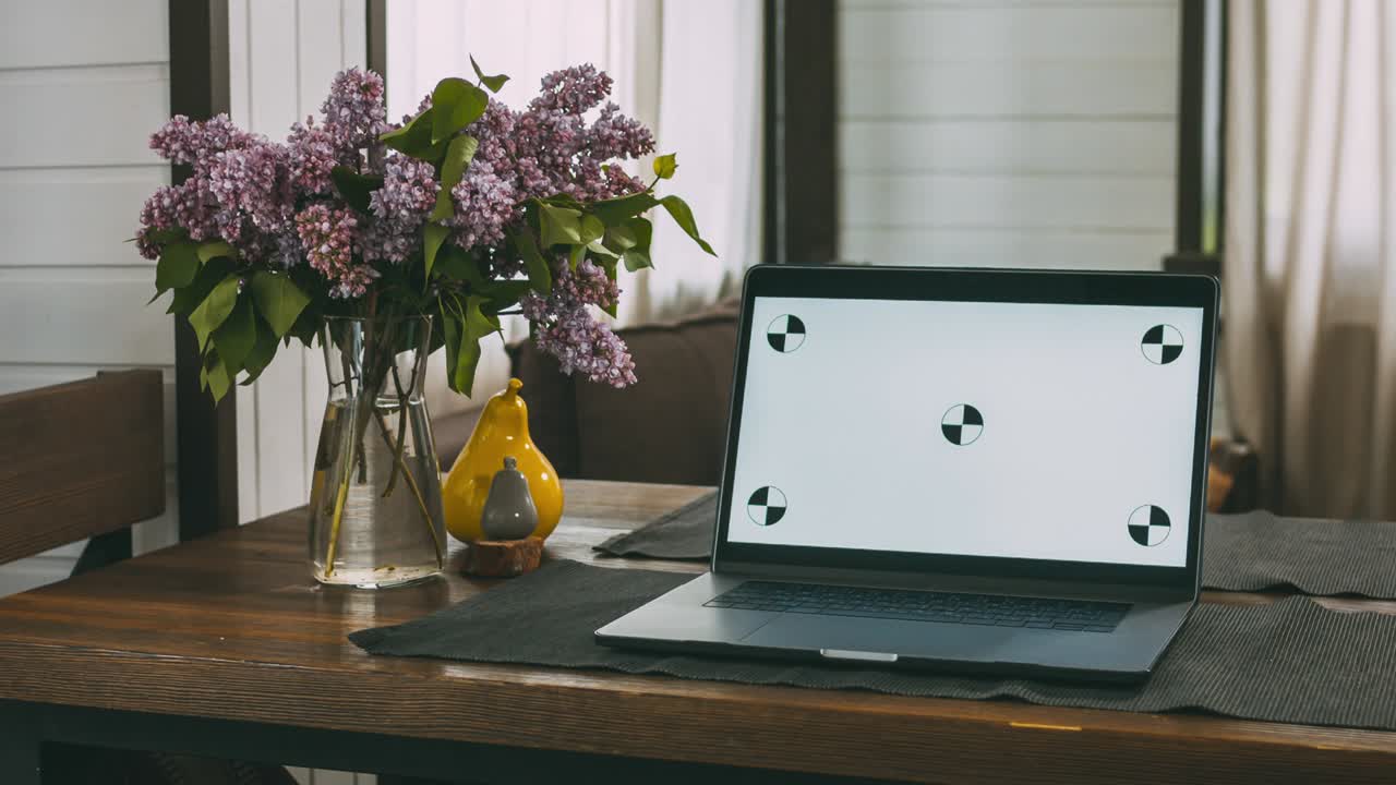 On a wooden table in the living room in the house is a laptop. A convenient and cozy place to work. Computer screen with dot tracking. Home furnishings. The interior of a residential building.