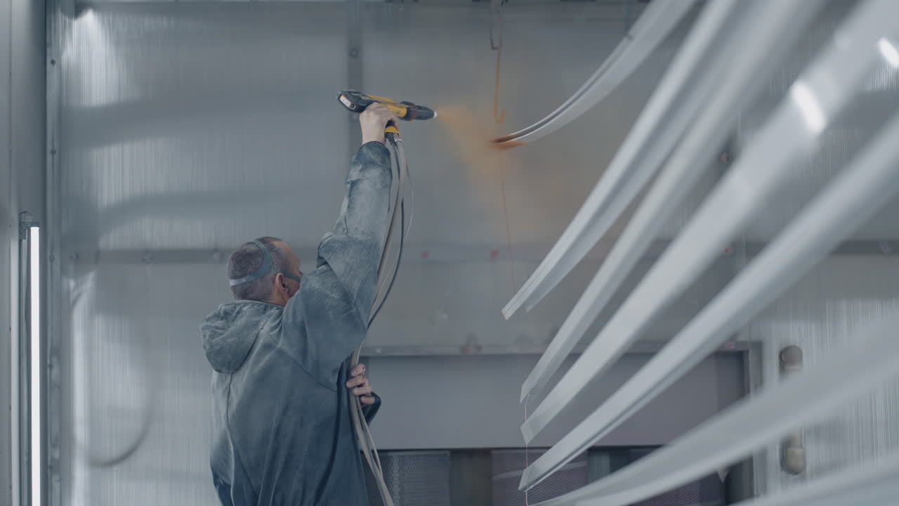 A man in a protective suit and mask painter sprays paint on the parts. Small business painting shop. Workshop for painting parts.