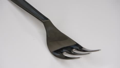 loopable selective focus view of a single metal fork spinning on white background.