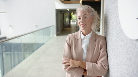 leaning against wall, smiling businesswoman in modern office hallway, copy space