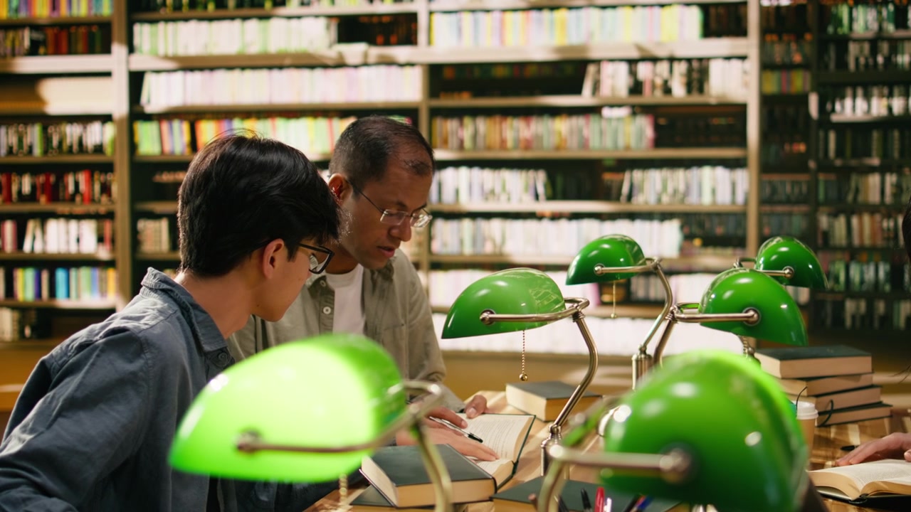 Mentor and student discussing research over open books at wooden library table