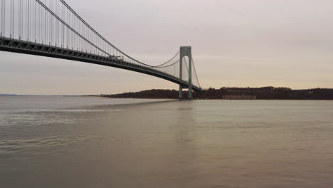 on a gray cloudy day, the drone takes off from shore parkway bike path, in view is a man fishing, the drone flies over to the hudson river, north of the verrazzano-narrows bridge in brooklyn, ny