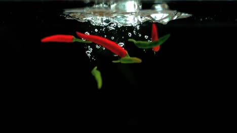 Animation-of-red-and-green-chilies-falling-in-the-water-against-black-background