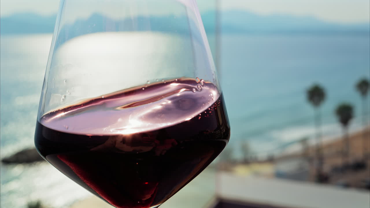Primo piano di una donna che fa roteare un bicchiere di vino rosso su un tavolo in una terrazza con vista mare