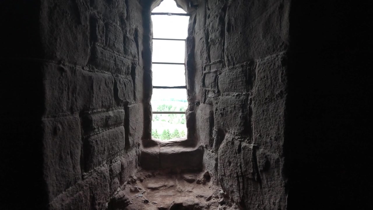 Movimento suave da câmera para frente dentro de uma masmorra ou fortaleza medieval escura, aproximando-se de uma janela antiga com grades de ferro e paredes de pedra