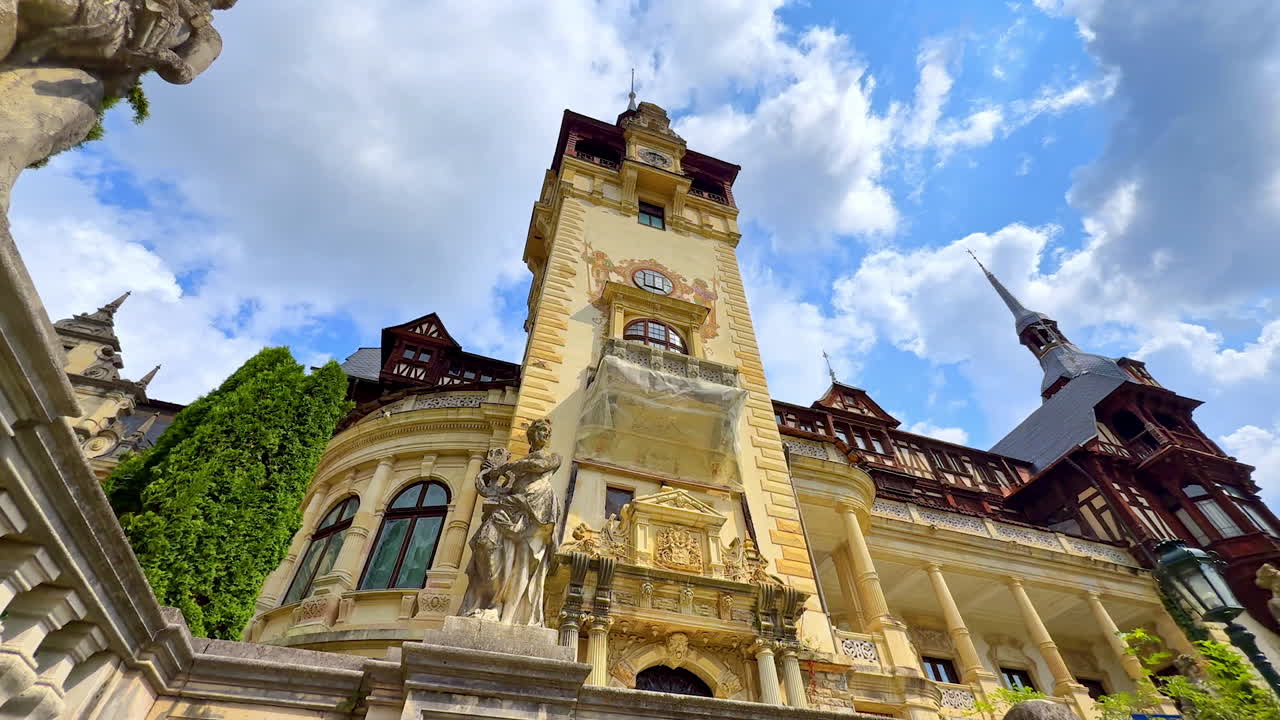 Beautiful statues and clock tower decorating the famous Peles Castle, Romania. Low angle view at the landmark on cloudy day