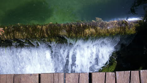 Pan-of-water-flowing-over-edge-with-plants-on-it-under-wooden-bridge