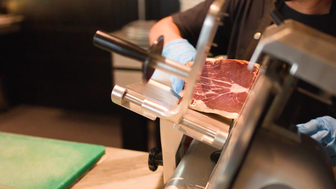 Chef che affetta salumi su affettatrice professionale