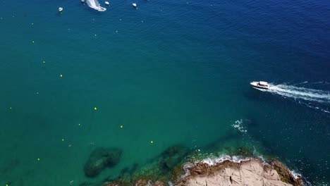 flying above a sailing boat next to the rocky coast of the mediterranean sea