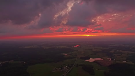 an aerial shot of a dim colourful sunset in a cloudscape above a rustic landscape