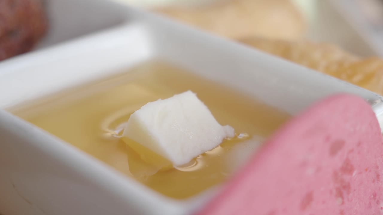 A white cube of food in a yellow liquid in a white bowl