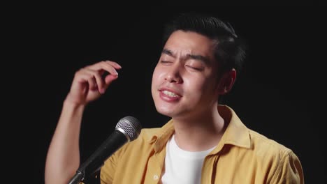 side view of asian man singer singing into microphone and hand snapping finger on black background