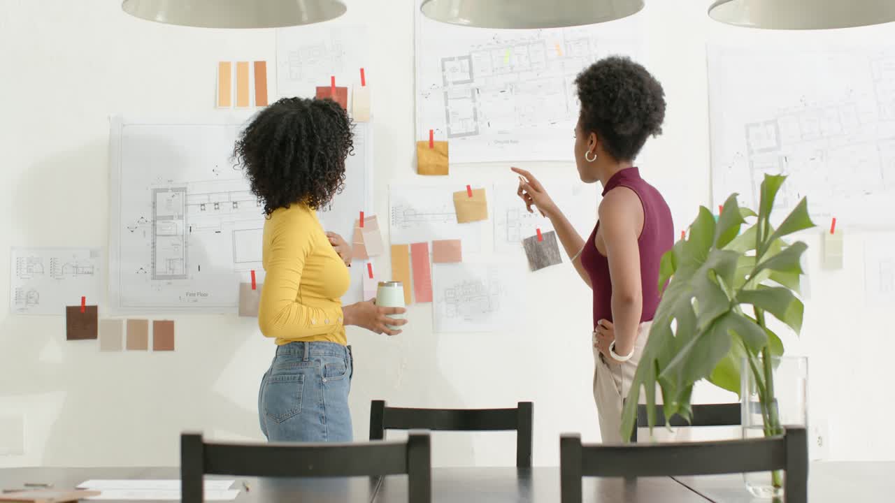 Diverse team left woman placing first note, gesturing and adjusting swatches on moodboard at studio