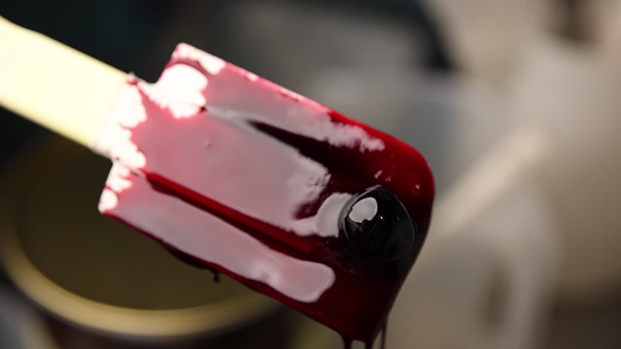 Sciroppo lucido di ciliegia che cola da una spatola rossa