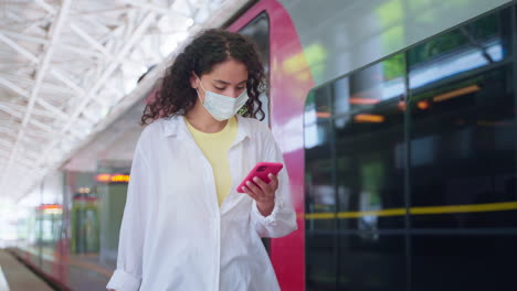 mujer en la estación de tren con máscara y usando el teléfono