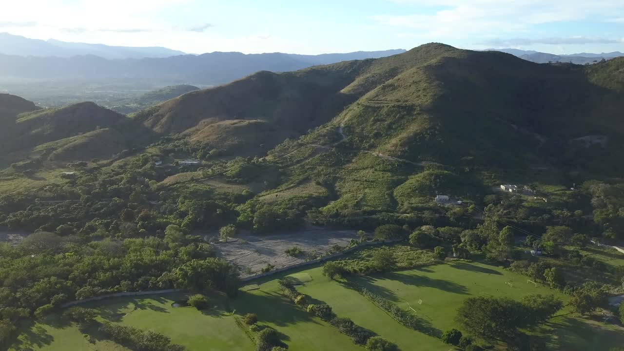Aerial shot of green field with trees and a big mountain