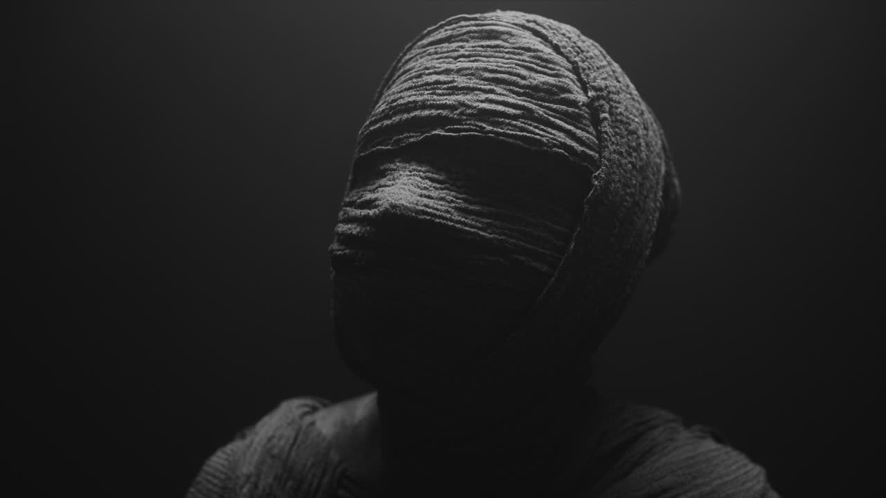 A mummy of a woman on a dark backdrop slowly rises her head