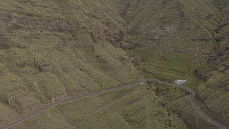 Panorama-drone-shot-of-a-car-driving-through-a-curvy-road-in-a-canyon-with-mountains