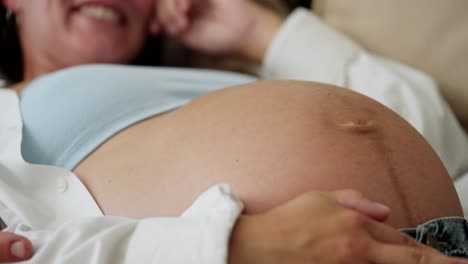 Close-up-of-happy-brunette-pregnant-woman-laughing-big-belly-of-pregnant-woman-stroking-with-hand-at-home