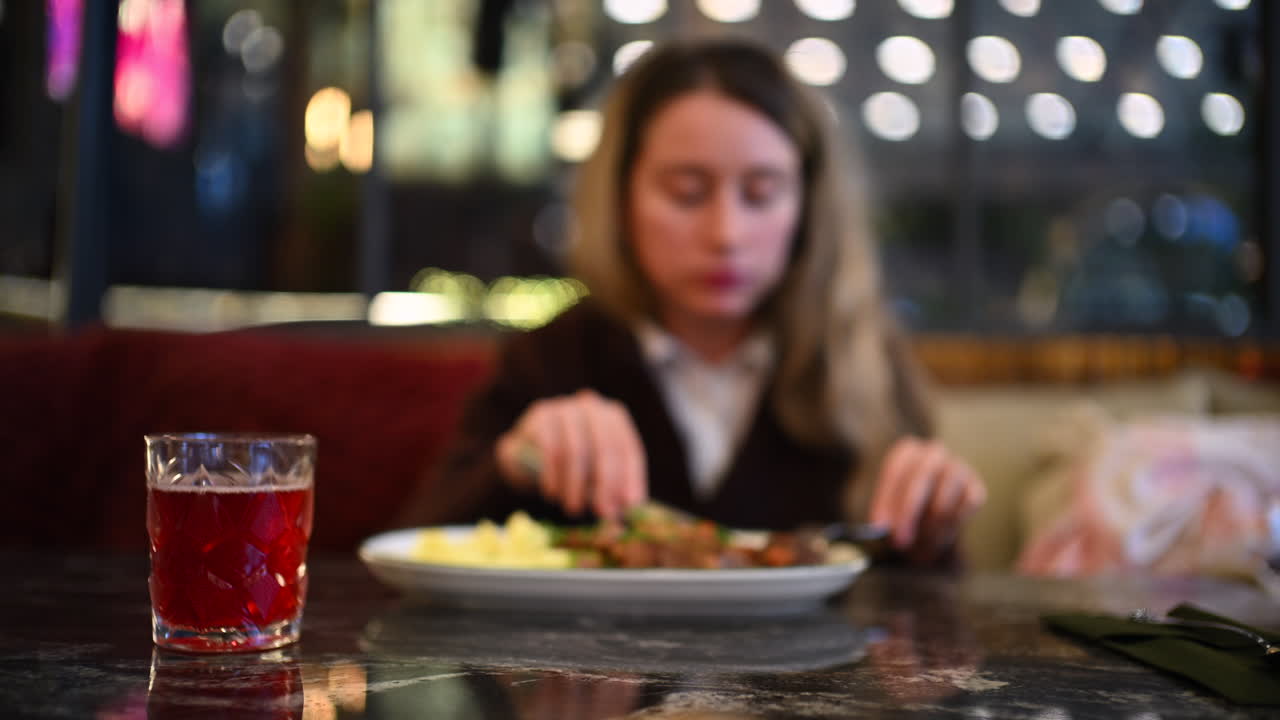 Woman eating mashed potatoes and meat at a restaurant table using fork and knife