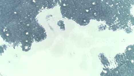 aerial drone bird's eye view over blue transparent clear ice with bubbles inside frozen lake at daytime