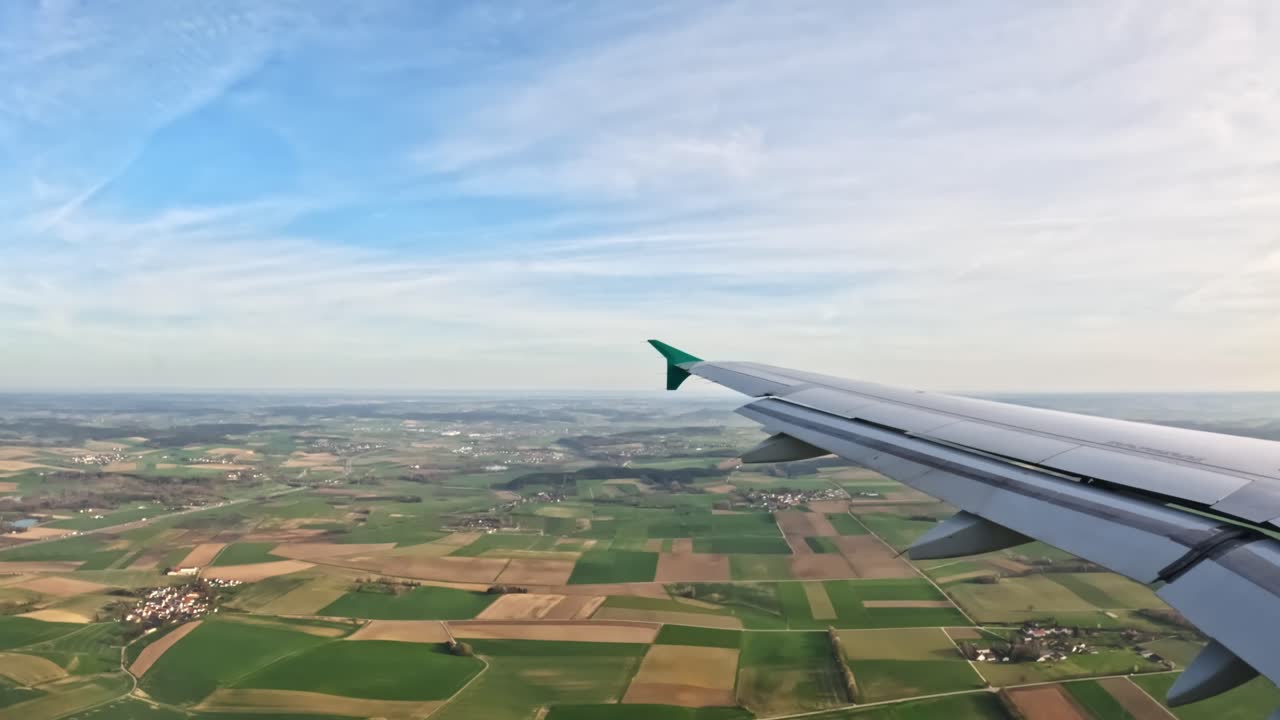 From the airplane window, fields stretch out below alongside the wing in clear view.