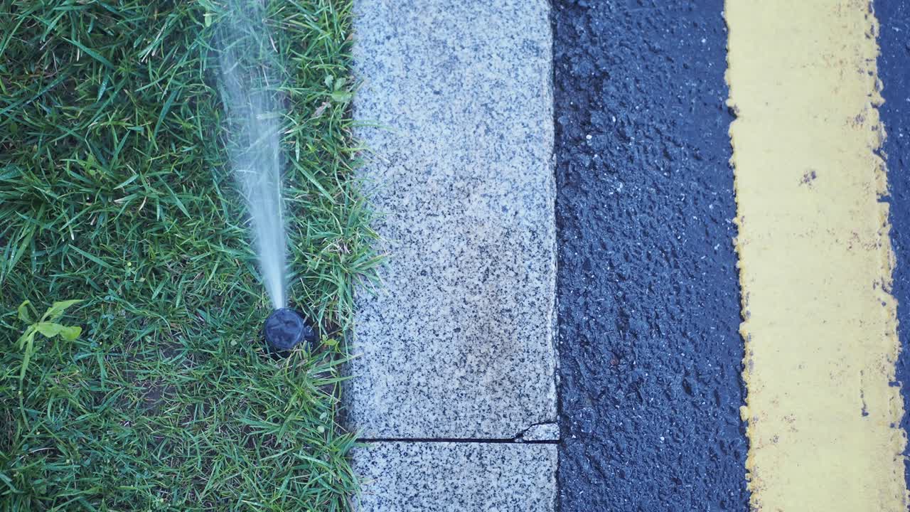 Watering Grass with Sprinkler on Sidewalk