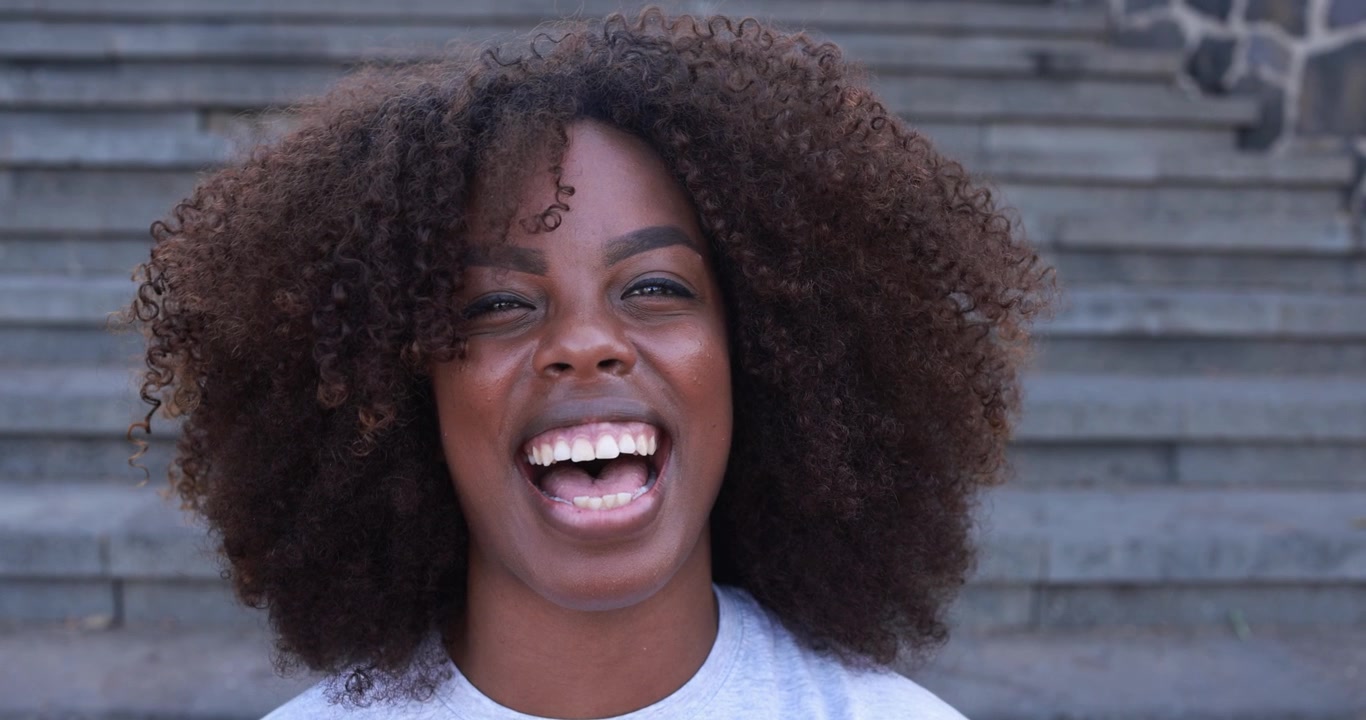 Glædesstrålende afroamerikansk kvinde med krøllet hår griner mod kameraet