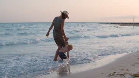 Cute-baby-boy-sitting-in-water-at-seaside.-Mother-and-son-walking-at-beach.