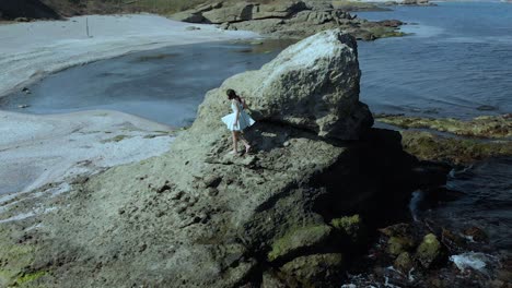 Girl-in-white-dress-climb-down-big-cliff-on-seashore