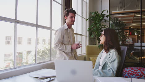 Two-young-creative-colleagues-talking-together-in-an-office-and-looking-out-of-the-window,-close-up