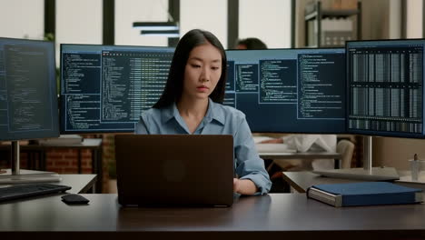 focused asian woman developer working on code in a multi-monitor office setup