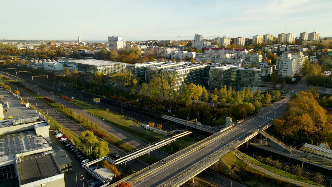 Ilmakuva junasta, joka liikkuu raiteilla sillan alla ohittaen Pommerin tiede- ja teknologiakeskus Gdynian rakennukset syksyisessä auringonnousussa.