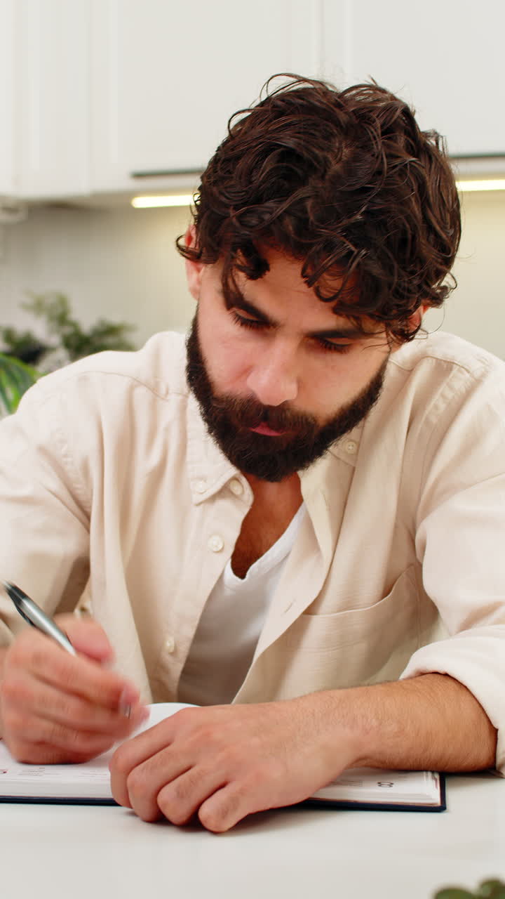 Indiano lendo uma carta oficial, colocando a mão no rosto, estressado com as finanças e escrevendo um plano de ação em um caderno
