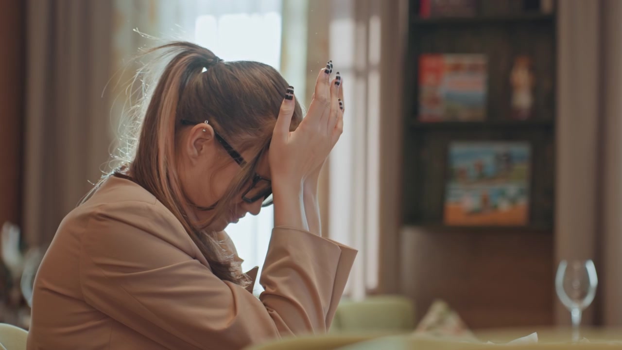 Donna in un caffè che accartoccia la carta, gesti espressivi, tensione facciale con la mano sulla fronte, mani che si passano tra i capelli, respiro lento, transizione dall'irritazione alla compostezza, luce calda ambientale, bistrò moderno.