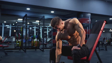 muscular athlete with a dumbbell. strong handsome sportsman without shirt pumping his arm biceps with sports equipment in the gym.