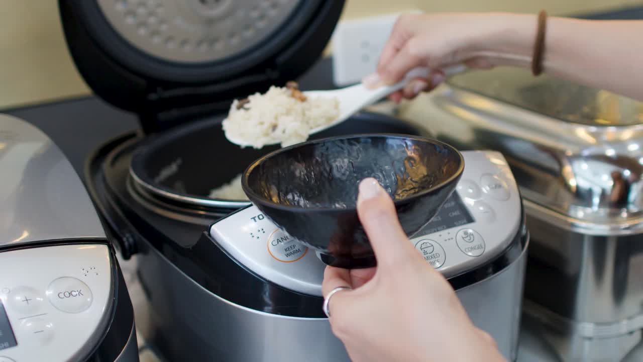 Close-up shot of hands using a white paddle to scoop rice into a black bowl