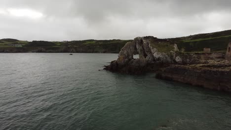 Reverse-aerial-view-flying-low-on-Traeth-Porth-Wen-Beach-bay-abandoned-brickwork-site-on-the-Irish-sea-coast