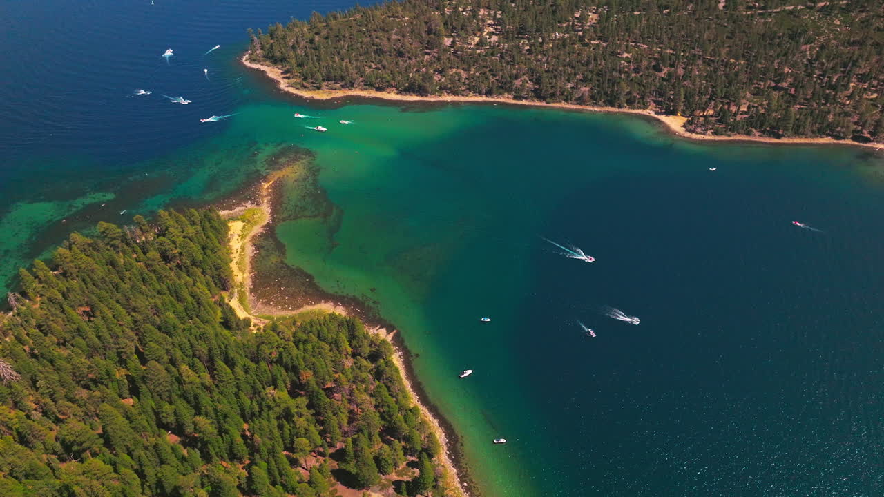 Speed boats and yachts sailing by the blue and turquoise waters of Lake Tahoe. Wooded shore with pine tree forest from aerial view.